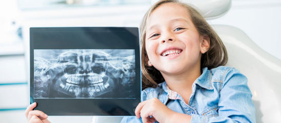 Girl at the dentist holding and x-ray and looking at the camera smiling